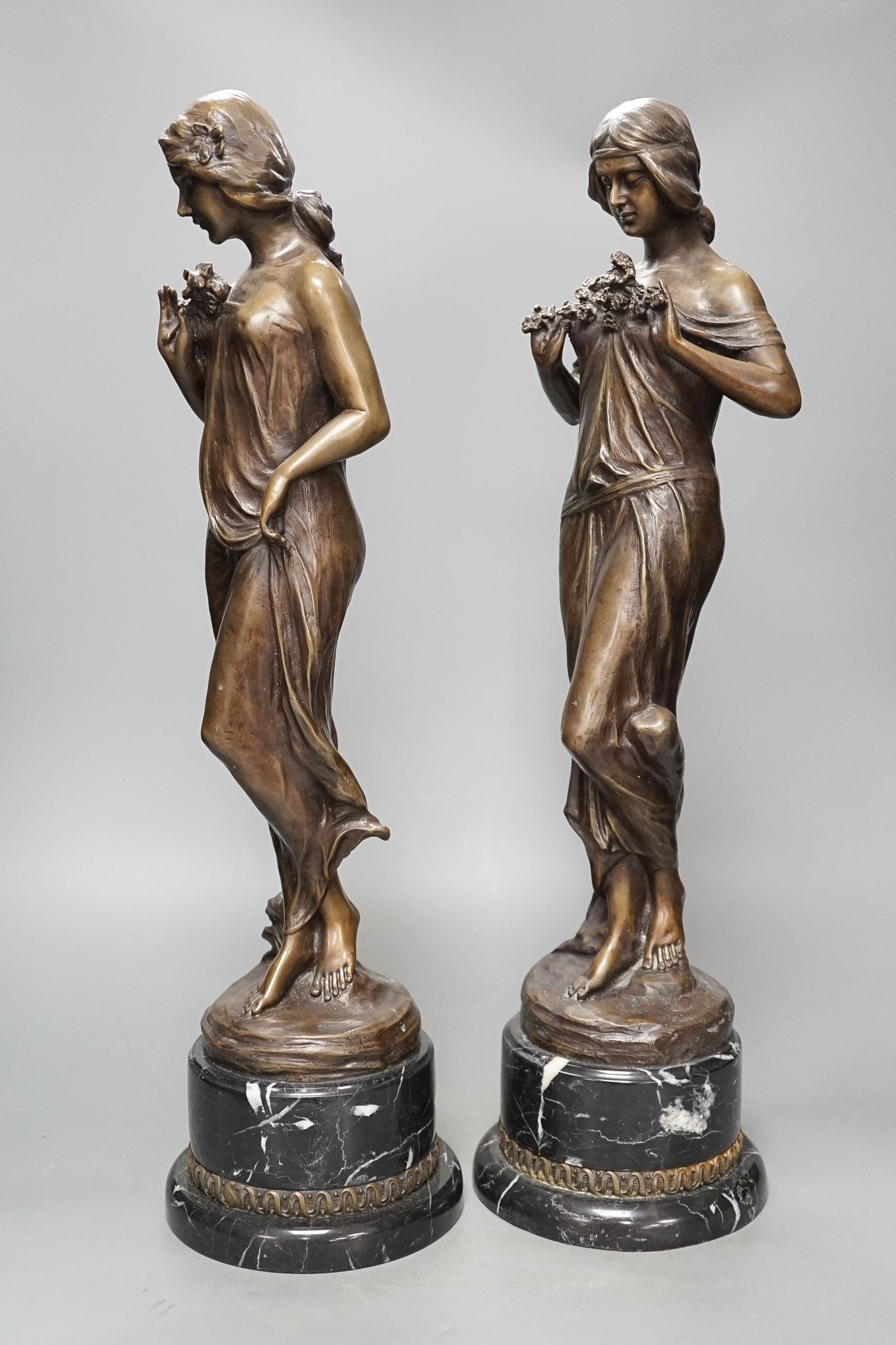 After Jean-Antoine Houdon, (French 1741-1828), a pair of bronze figures of lady’s holding flowers, on marble bases, 52cm